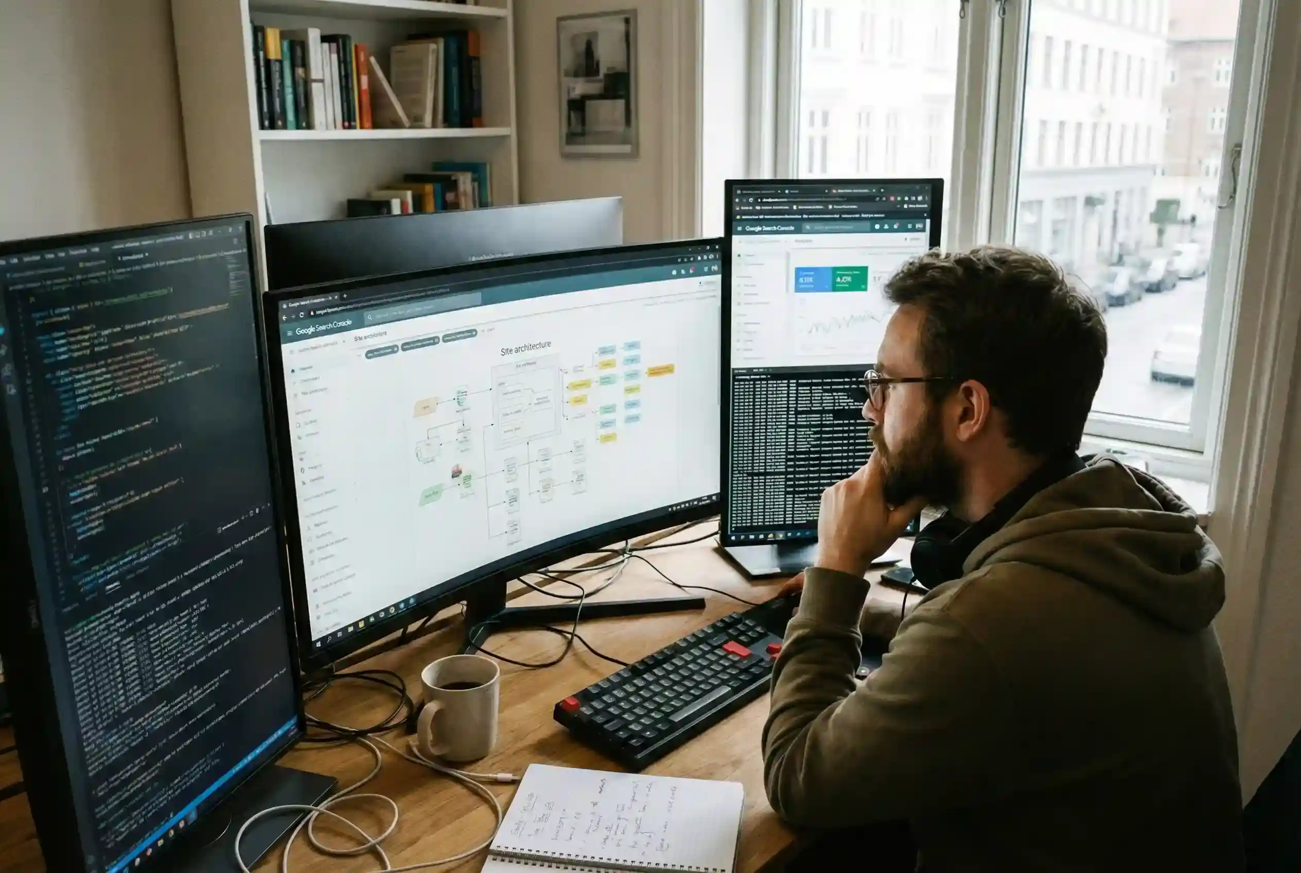 A technical SEO web design specialist working at a high-end workstation, analyzing site architecture diagrams and backend code across multiple monitors to ensure search engine crawlability.